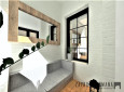 Projekt salonu z sofą, białą cegła na ścianie oraz prostokątnym lustrem w drewnianej ramie