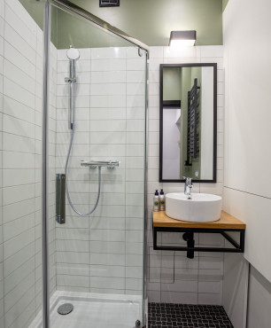 Łazienka z prysznicem narożnym z drzwiami wahadłowymi, z ciemnymi płytkami na podłodze i białymi na ścianie