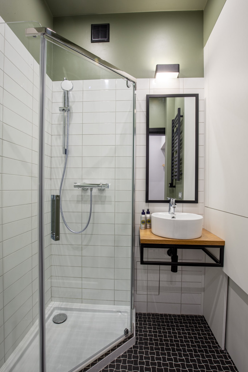 Łazienka z prysznicem narożnym z drzwiami wahadłowymi, z ciemnymi płytkami na podłodze i białymi na ścianie