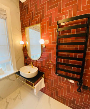 Łazienka hotelowa z czerwonymi płytkami na ścianie oraz szafką wiszącą z umywalką nablatową
