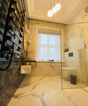 Mała, nowoczesna łazienka hotelowa z prysznicem, białymi płytkami gresowymi oraz na jednej ścianie z czarnymi