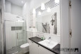 Wysoka łazienka z prysznicem z drzwiami przesuwnymi, szafką stojącą z czarnym blatem oraz umywalką nablatową