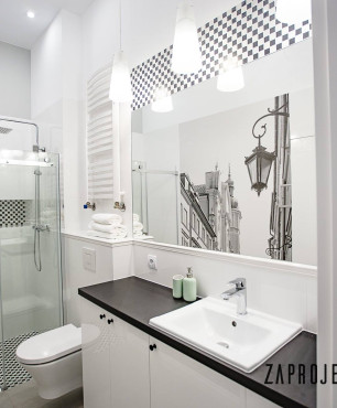 Wysoka łazienka z prysznicem z drzwiami przesuwnymi, szafką stojącą z czarnym blatem oraz umywalką nablatową