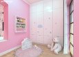 Pokój dziecięcy z różowym kolorem ścian oraz białą szafą w zabudowie