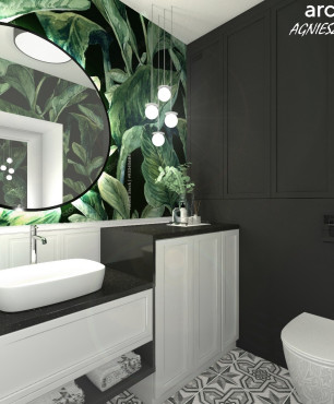 Projekt łazienki z efektem botanicznym na ścianie oraz z okrągłym lustrem w czarnej ramie
