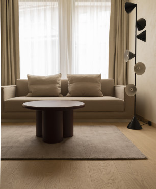 Klasyczny salon z bezową sofą, okrągłym stolikiem kawowym, lampą stojącą oraz jasnym dywanem