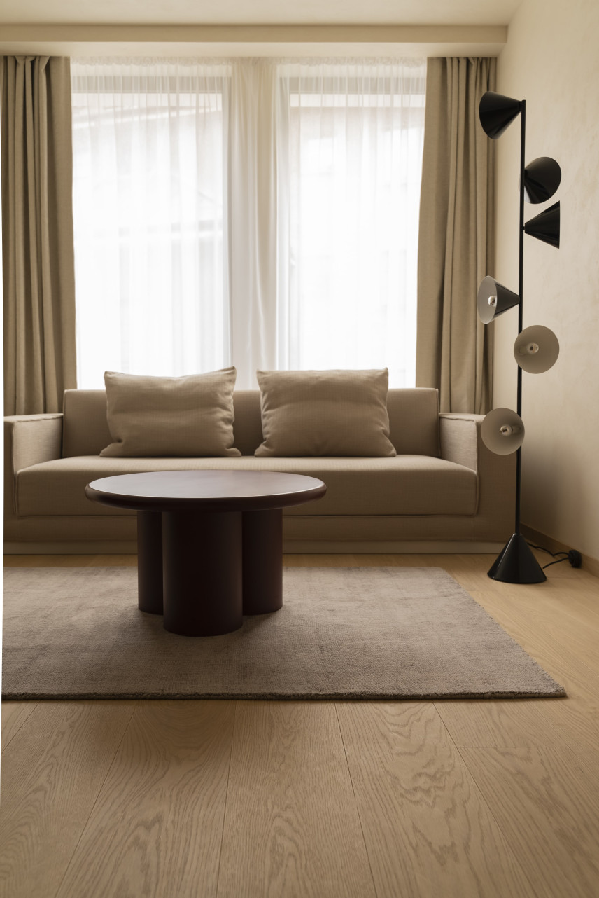 Klasyczny salon z bezową sofą, okrągłym stolikiem kawowym, lampą stojącą oraz jasnym dywanem