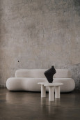 Salon w stylu loft z betonową ścianą, kremową sofą oraz stolikiem kawowym