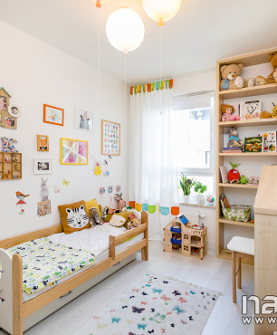 Pokój dziecięcy z białym kolorem ścian, łóżkiem, komodą oraz szafką na zabawki i książki